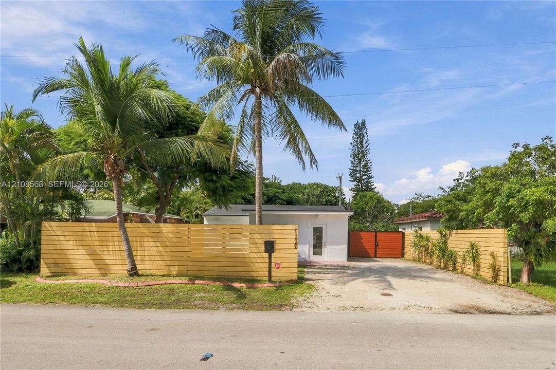Exterior featuring horizontal wood slat fencing, a gravel driveway, an opaque-finish detached structure, and mature palm trees