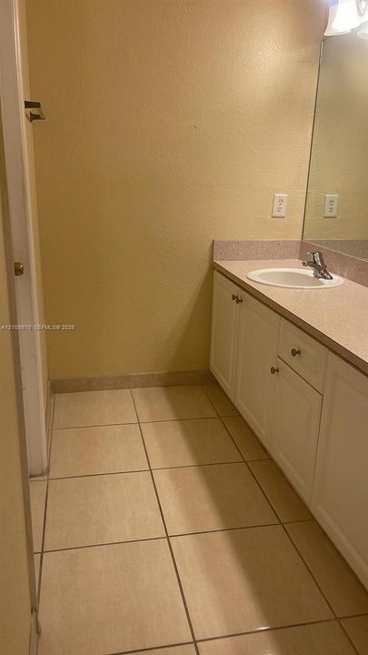 Bathroom vanity featuring white cabinetry, a solid-surface countertop, an integrated sink, and tile flooring