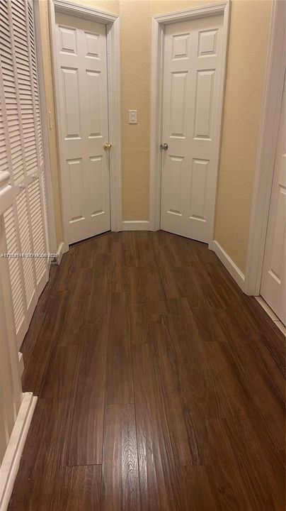 Wood-finish flooring, two six-panel interior doors, and white louvered closet doors