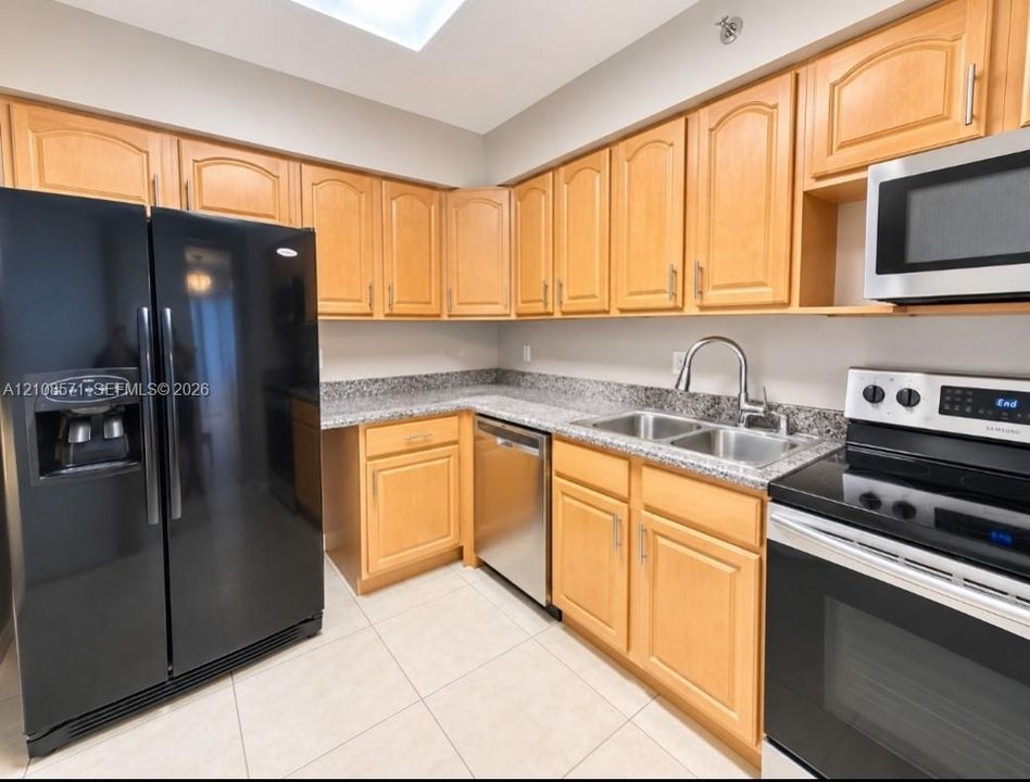 Kitchen featuring light-finish cabinetry, stone-surface countertops, stainless steel appliances, a dual-basin sink, and tile flooring