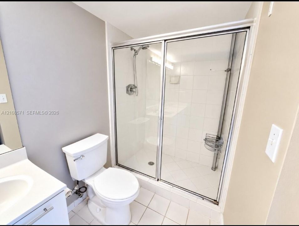Shower enclosure featuring a chrome hand-held shower head, tiled walls, and sliding glass doors, paired with a white vanity and porcelain toilet