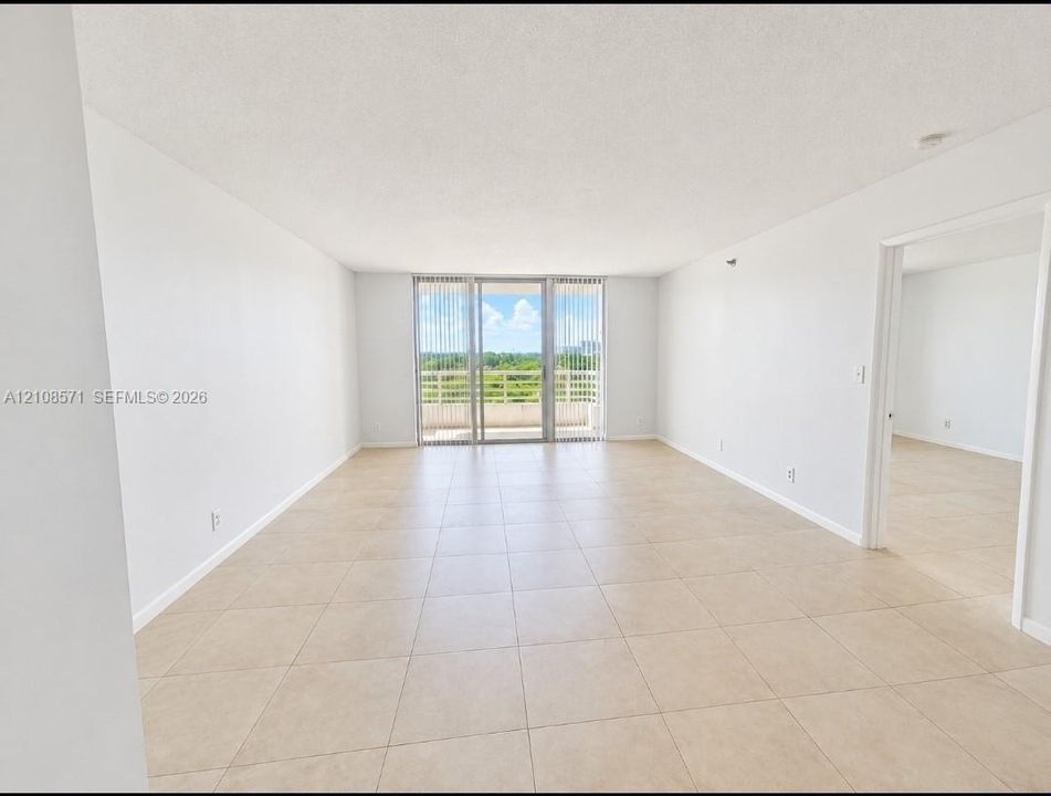 Neutral interior featuring light-toned tile flooring, floor-to-ceiling glass sliding doors, and a private balcony