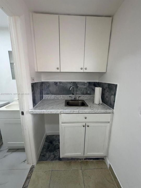 Built-in white cabinetry, stone-patterned laminate countertop, stainless steel drop-in sink with a dual-handle faucet, and decorative tile backsplash