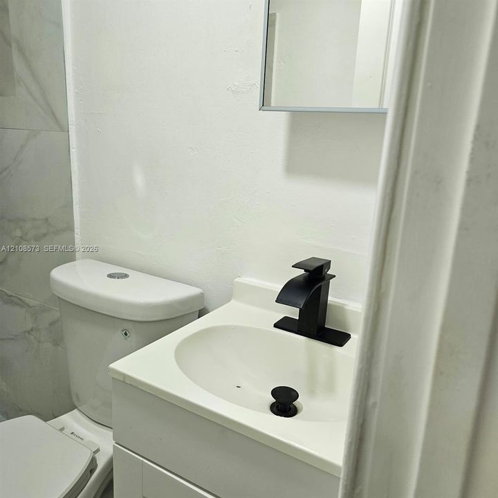 Modern vanity with an integrated sink, matte black waterfall faucet, white cabinetry, and large-format tile wall detailing