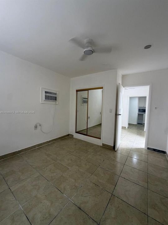 Room featuring tile flooring, ceiling fan with integrated lighting, built-in closet with sliding mirrored doors, and wall-mounted air conditioning unit