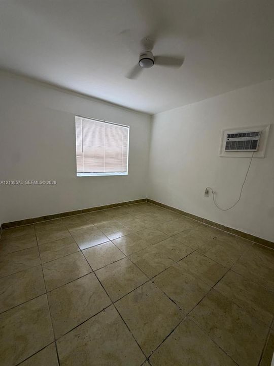 Room featuring large-format tile flooring, a neutral color palette, a window with integrated blinds, a wall-mounted air conditioning unit, and a ceiling fan