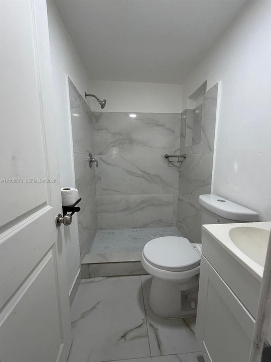 Walk-in shower with floor-to-ceiling veined tile surround, porcelain floor tiling, vanity with integrated basin, and brushed-finish metal fixtures