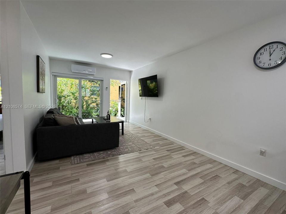 Wood-finish flooring, sliding glass door, wall-mounted ductless climate control unit, and flush-mount lighting