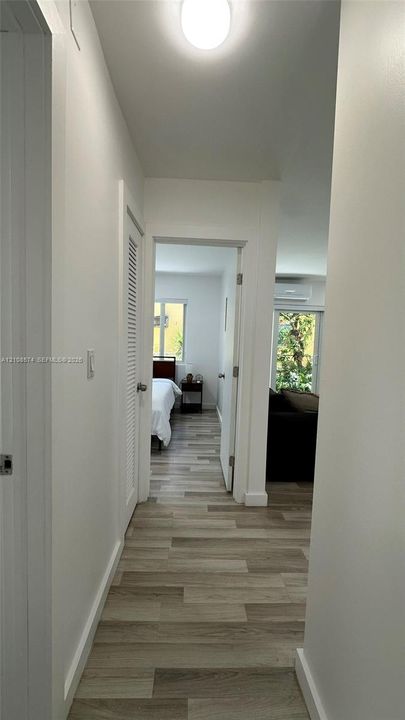 Hallway featuring wood-finish flooring, white walls, louvered door access, and a flush-mount ceiling light fixture