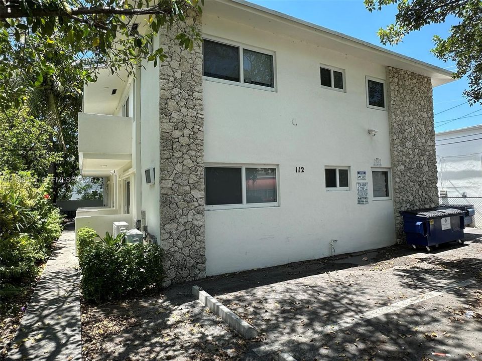 Multi-story exterior featuring a smooth stucco finish, natural stone accents, horizontal sliding windows, and a dedicated paved parking area