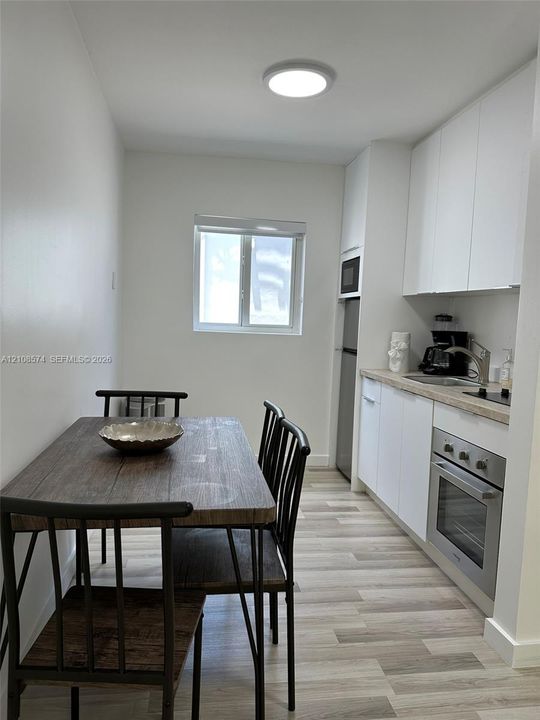 Kitchen featuring white flat-panel cabinetry, light-toned countertop, stainless steel oven, integrated microwave, and wood-finish flooring
