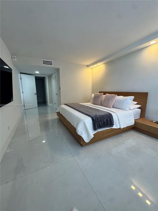 Large-format tile flooring, recessed ceiling lighting, and integrated wall-to-wall wood-finish headboard with matching side tables