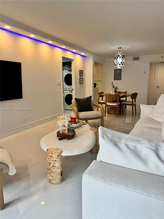 Interior space featuring large-format tile flooring, recessed ceiling lighting with integrated colored accent strips, and a designated laundry area equipped with a stacked washer and dryer