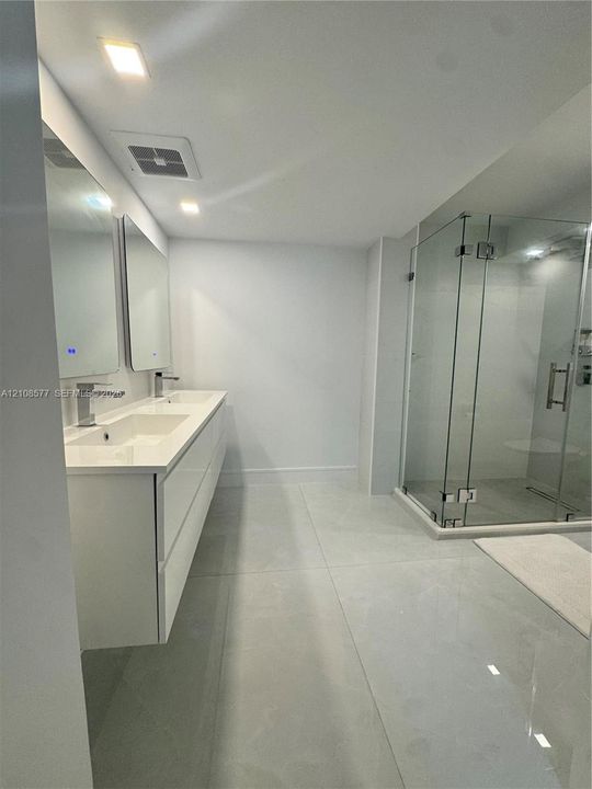 Floating dual-sink vanity with a solid-surface countertop, glass-enclosed shower, polished large-format floor tile, and rectangular wall-mounted mirrors