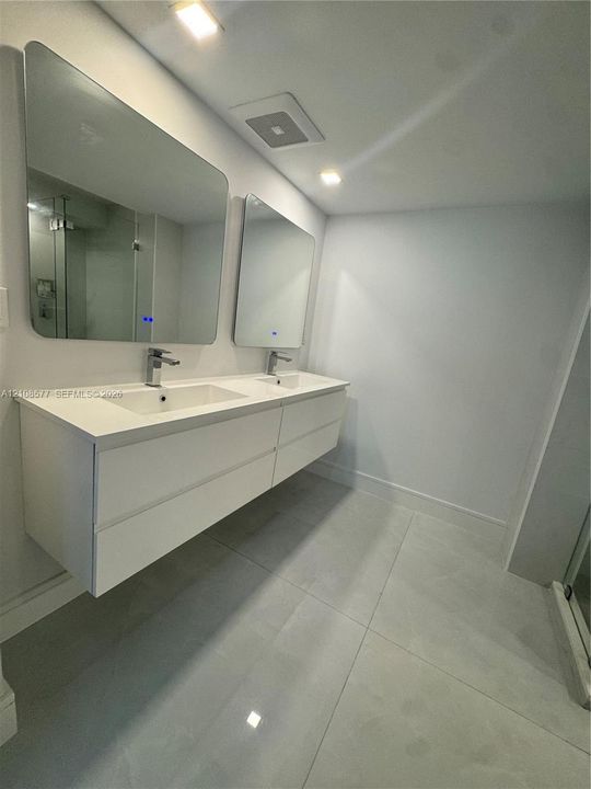 Floating double vanity with a stone countertop, integrated sinks, chrome faucets, and two illuminated mirrors, complemented by large-format tile flooring