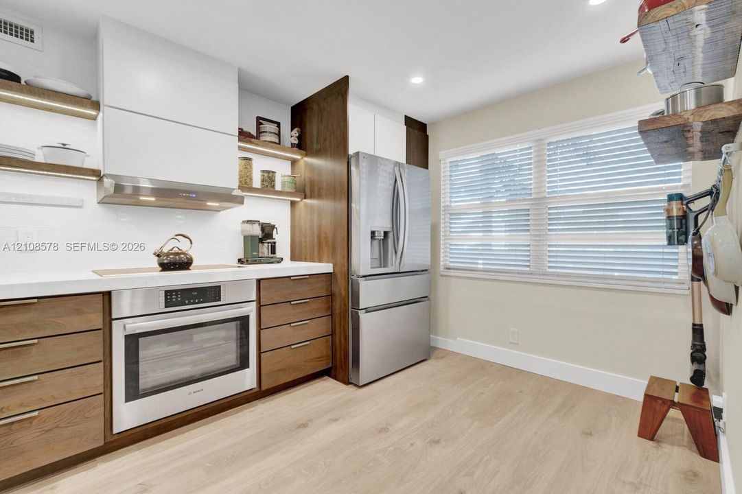 Kitchen featuring wood-finish cabinetry, white slab countertops, stainless steel appliances, open wood shelving, and wood-finish tile flooring