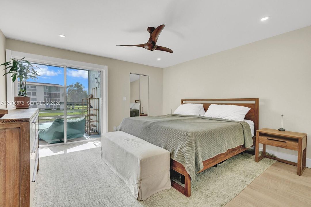 Sliding glass door access to a private balcony, wood-finish flooring, recessed lighting, and a multi-blade ceiling fan
