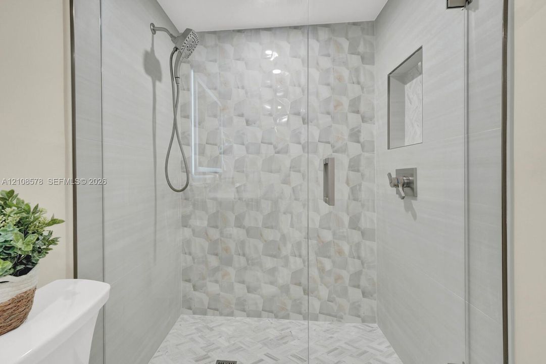 Walk-in shower featuring a frameless glass door, geometric patterned accent tile, built-in wall niche, herringbone floor tile, and multi-setting handheld shower head