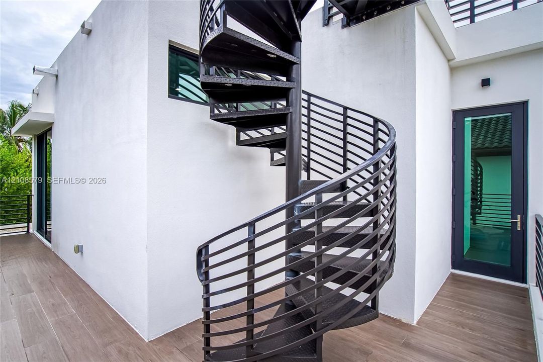 Black metal spiral staircase featuring open-riser treads, wood-finish flooring, and a glass-paneled entry door