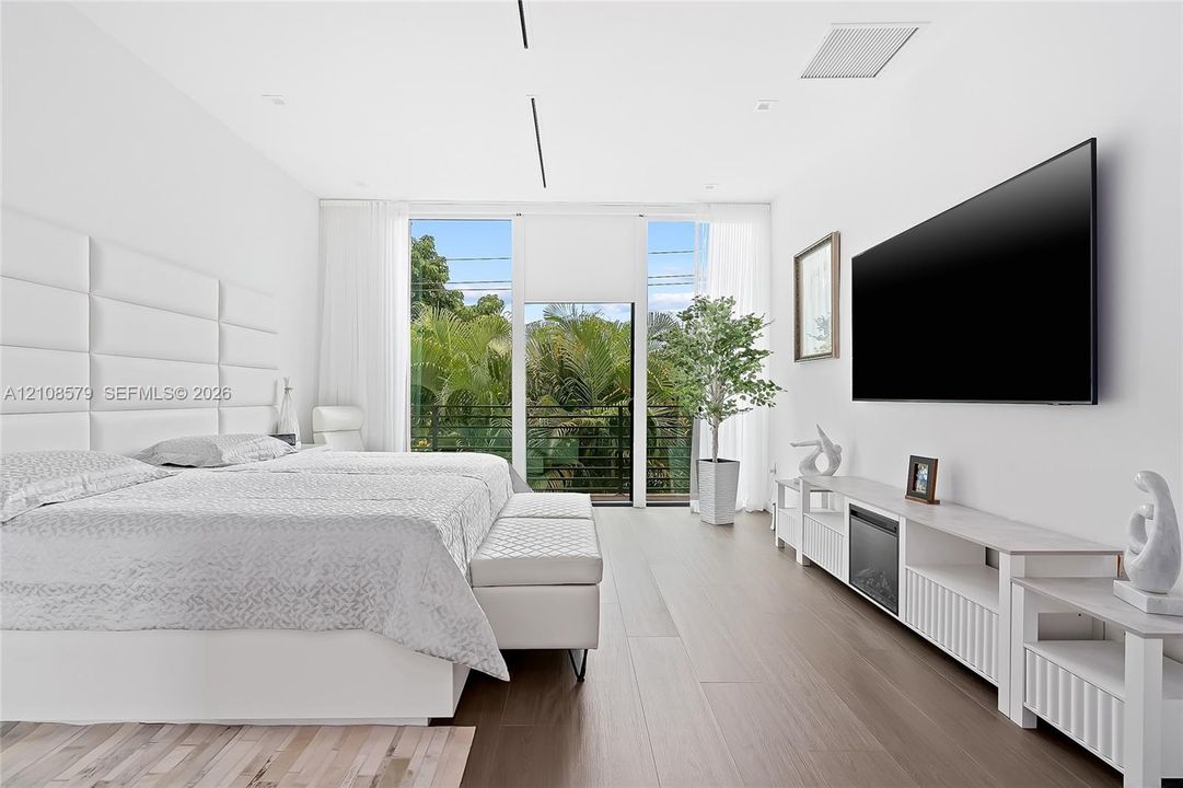 Wood-finish flooring, floor-to-ceiling windows with outdoor balcony access, and a built-in upholstered headboard wall paneling