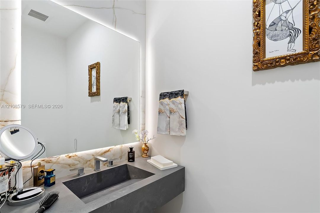Floating vanity with a charcoal-toned integrated sink, stone-finish backsplash, expansive frameless mirror with integrated LED backlighting, and modern polished metal fixtures
