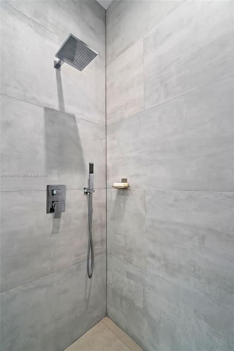 Walk-in shower featuring large-format stone-finish wall tile, a rainfall showerhead, a separate handheld shower sprayer, and a built-in recessed shelf