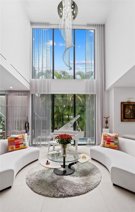Double-height living area featuring floor-to-ceiling glass windows, a statement modern chandelier, and large-format tile flooring