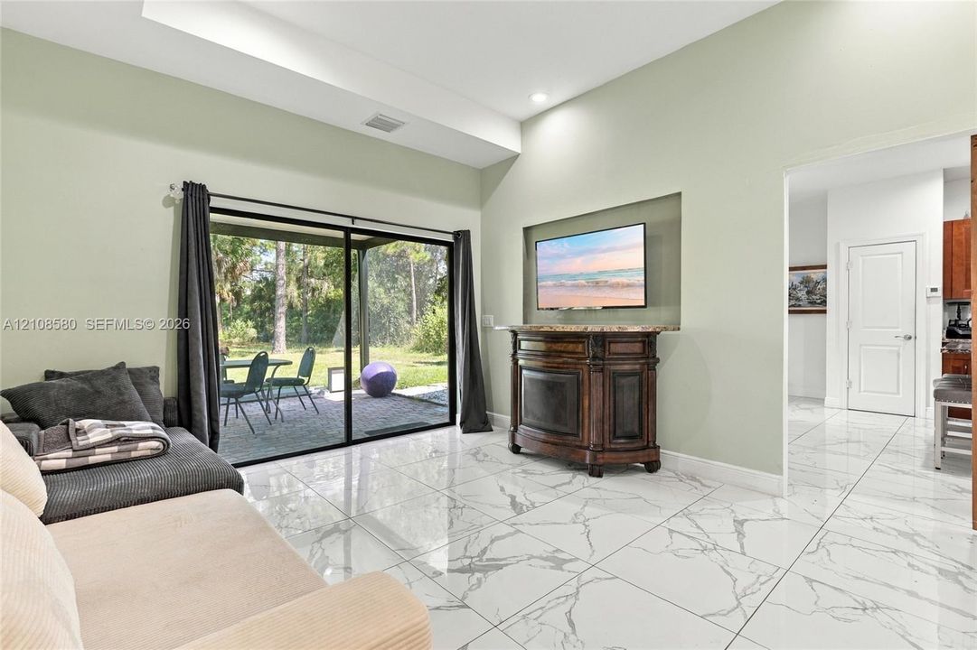 Vaulted ceilings, large-format tile flooring with a marble-style finish, recessed wall niche, and sliding glass doors with access to a paved patio