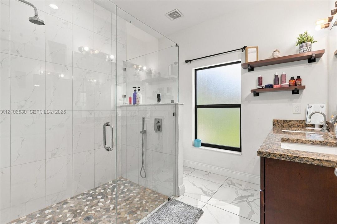 Walk-in shower featuring glass paneling, floor-to-ceiling tile surround, and a pebble-stone floor finish