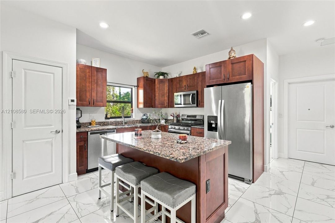 Kitchen featuring stained wood cabinetry, stone-surface countertops, center island with seating, stainless steel appliances, and large-format tile flooring