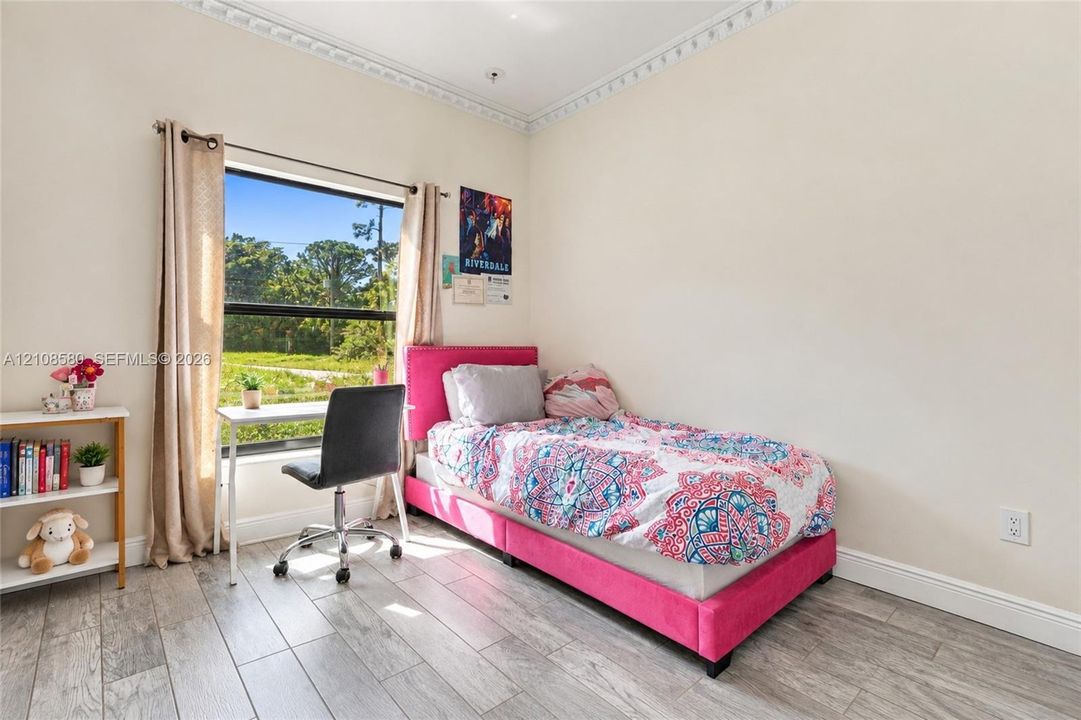 Room featuring wood-finish flooring, decorative crown molding, and a large window with natural light
