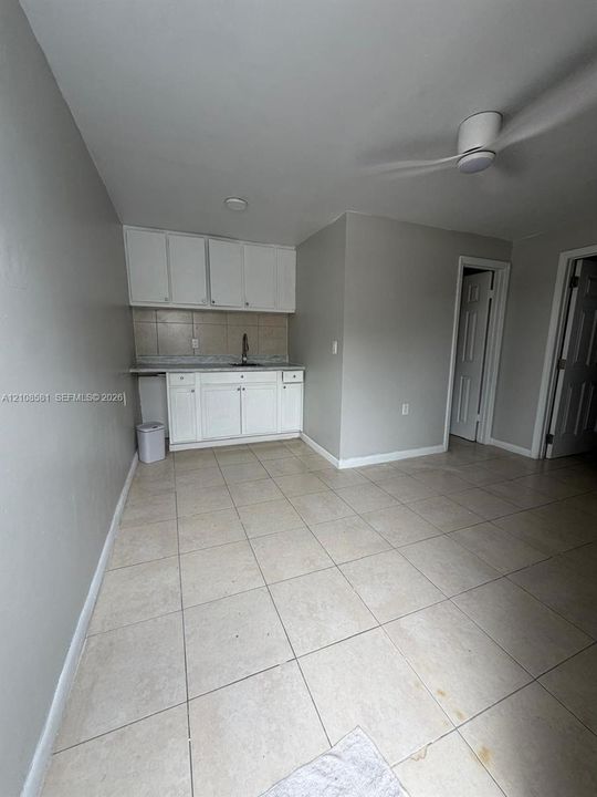 Kitchenette featuring white cabinetry, a neutral tiled backsplash, a built-in sink with a faucet, neutral floor tiling, and a ceiling-mounted fan
