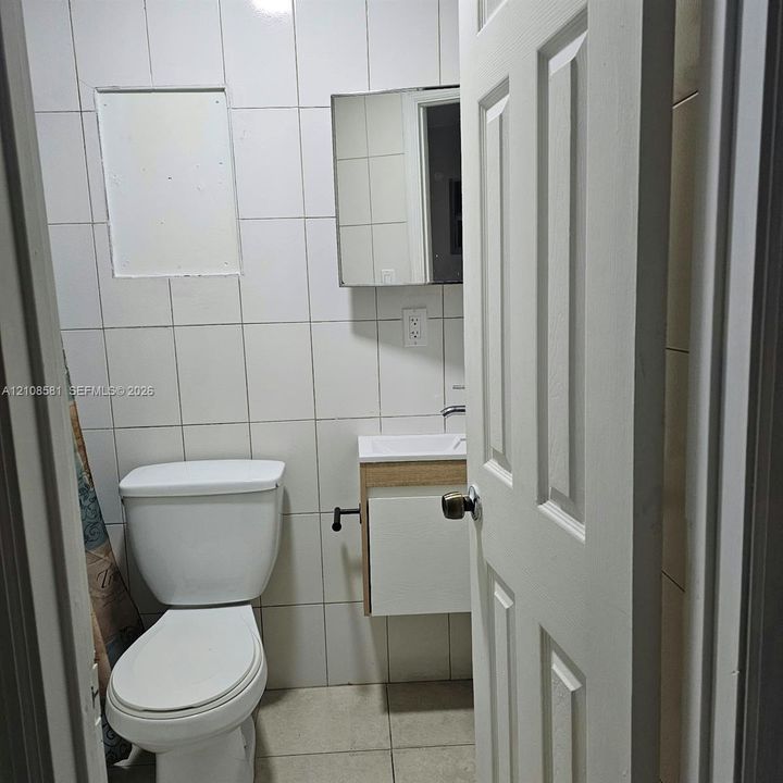 Bathroom featuring full-height ceramic wall tiling, a wall-mounted vanity with a rectangular basin, and a recessed medicine cabinet
