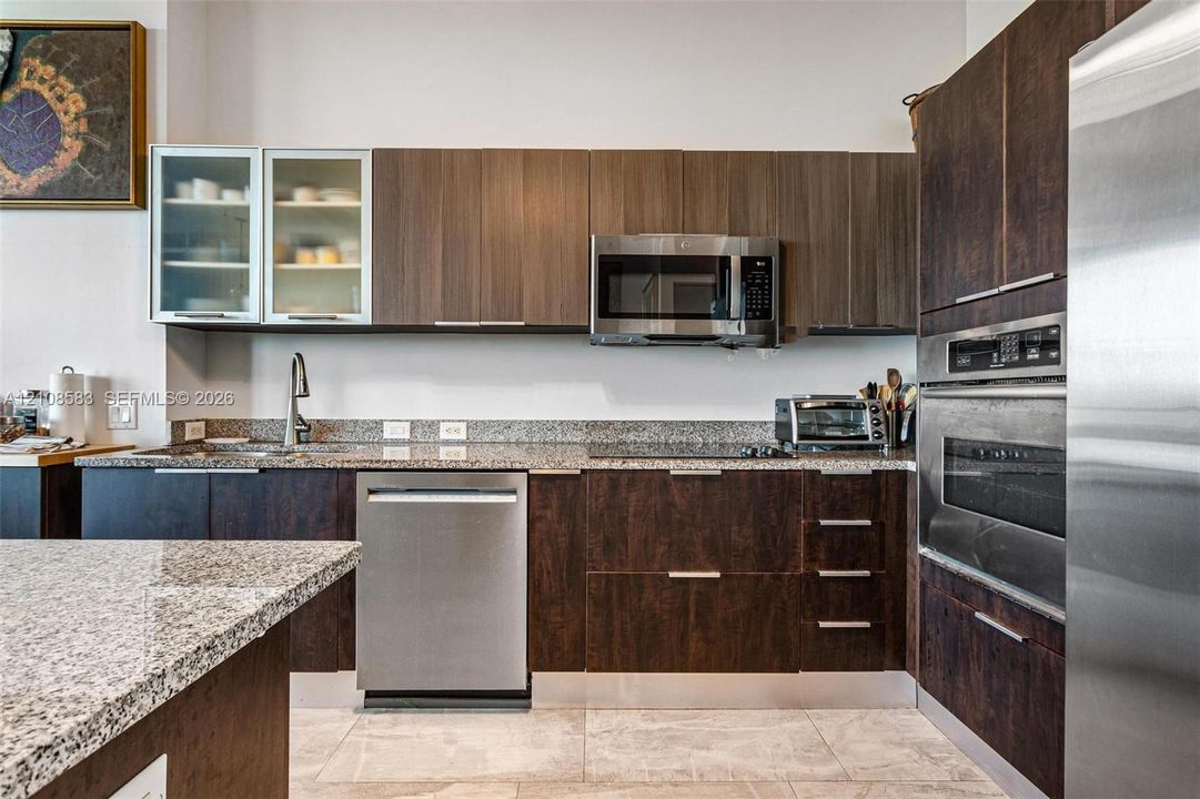 Kitchen featuring flat-panel wood cabinetry, speckled stone countertops, stainless steel appliances, glass-front upper cabinets, and tile flooring
