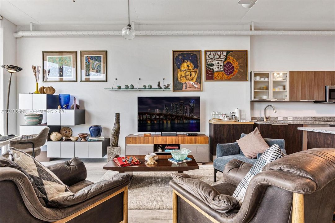 Open-concept interior featuring exposed industrial piping, flat-panel cabinetry with glass-front uppers, and solid-surface countertops