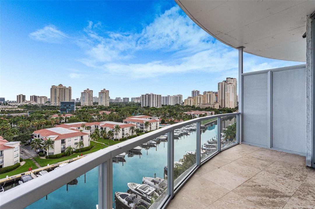 Covered balcony featuring stone flooring and a glass-paneled railing overlooking the waterway and marina