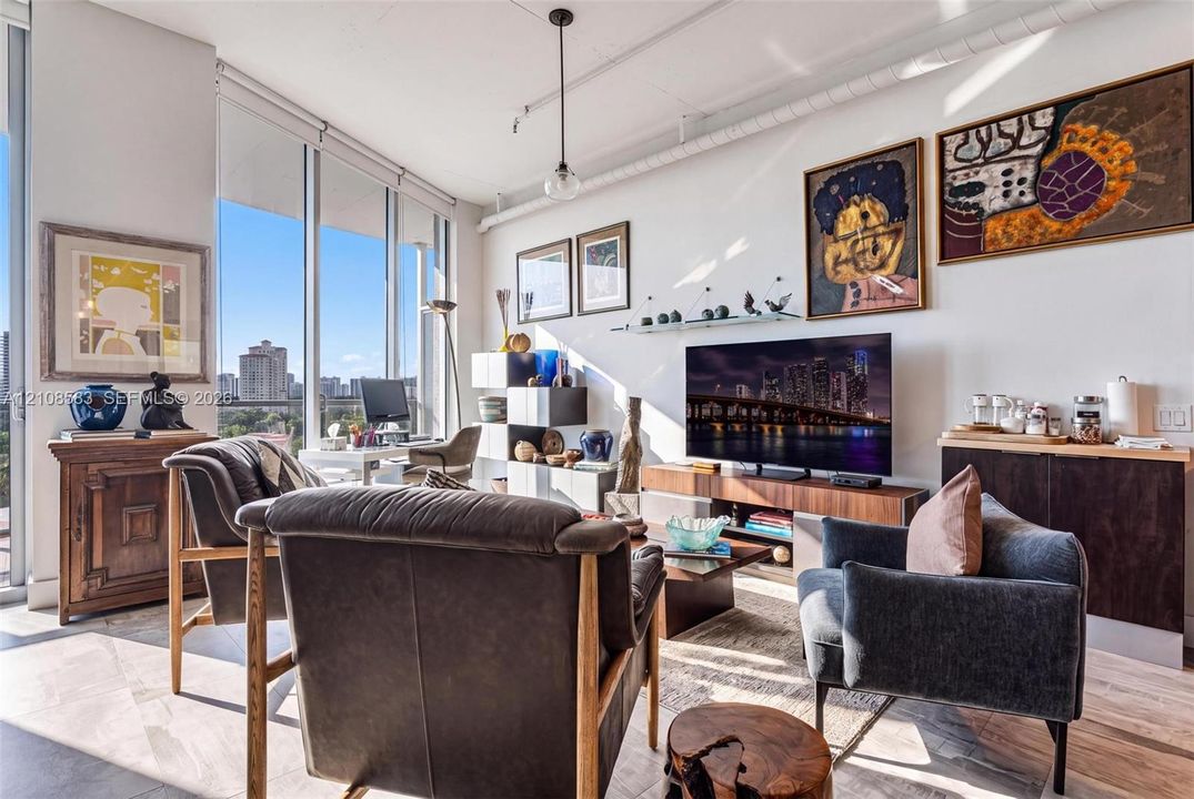 Living area featuring floor-to-ceiling windows, high ceilings, exposed ductwork, wood-finish flooring, and a built-in dark wood-finish cabinet