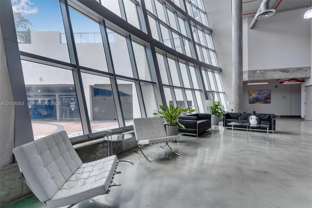 Floor-to-ceiling angled glass curtain wall, polished concrete flooring, exposed industrial structural column, and high-clearance ceilings