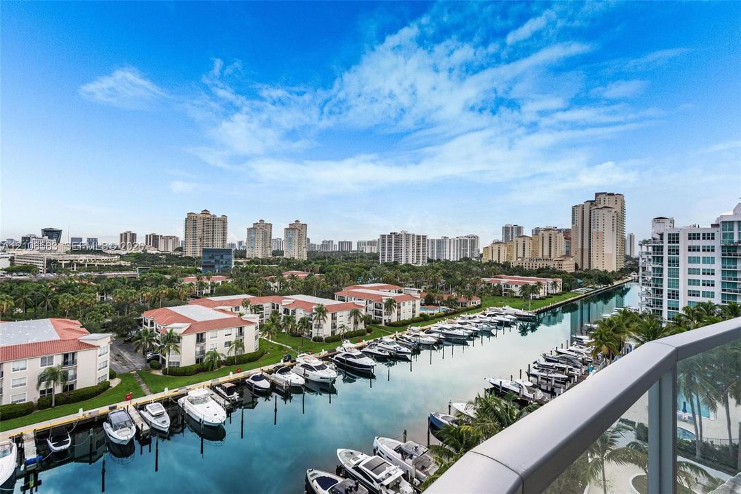 Balcony with glass railings overlooking a canal, private boat slips, multi-story buildings, and a cityscape backdrop
