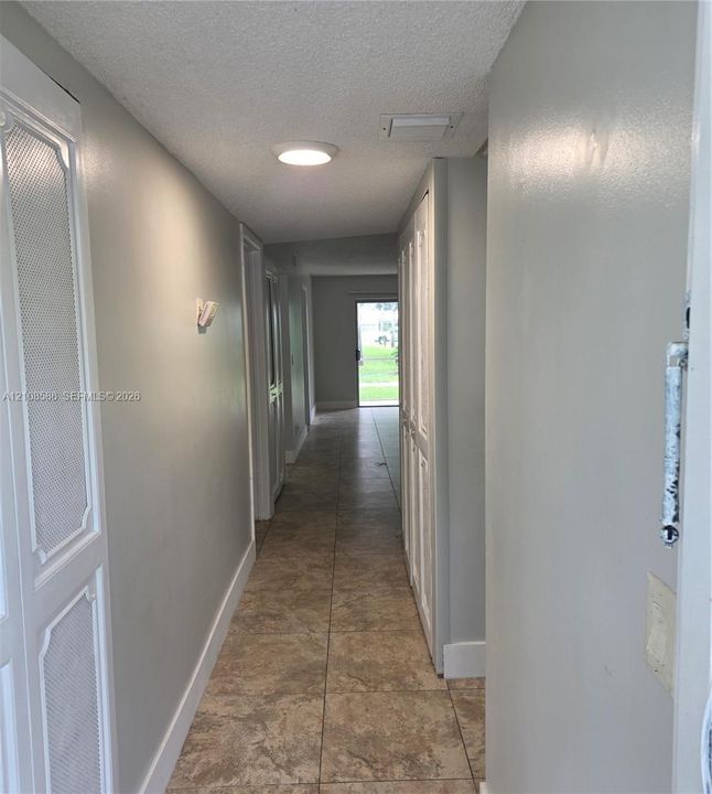 Hallway featuring large-format ceramic tile flooring, built-in floor-to-ceiling storage cabinetry with louvered doors, and flush-mount ceiling lighting
