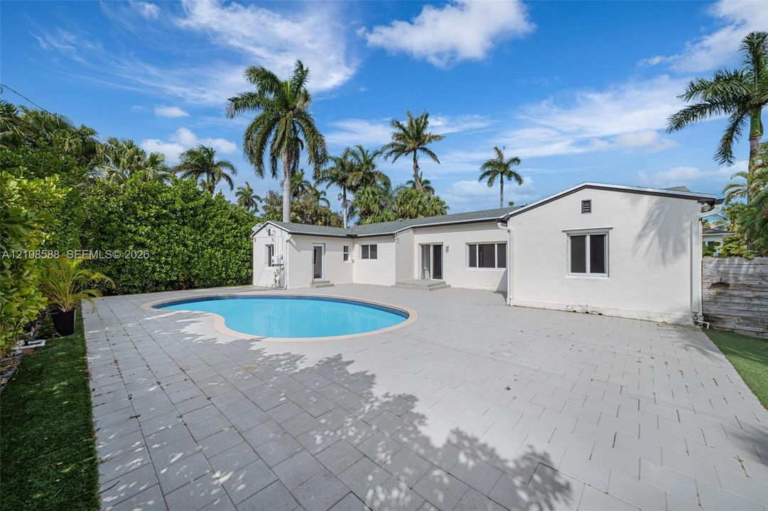 Exterior backyard featuring a concrete paver patio, kidney-shaped swimming pool, and mature palm trees