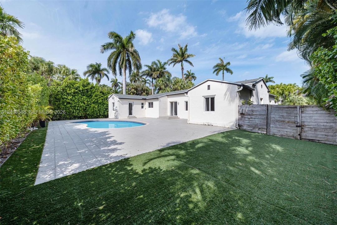 Backyard featuring a swimming pool, large paver patio, synthetic turf lawn, and perimeter wood fencing