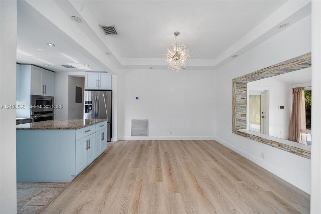 Wood-finish flooring, tray ceiling with recessed lighting, central crystal-style chandelier, and stone-accented interior wall opening
