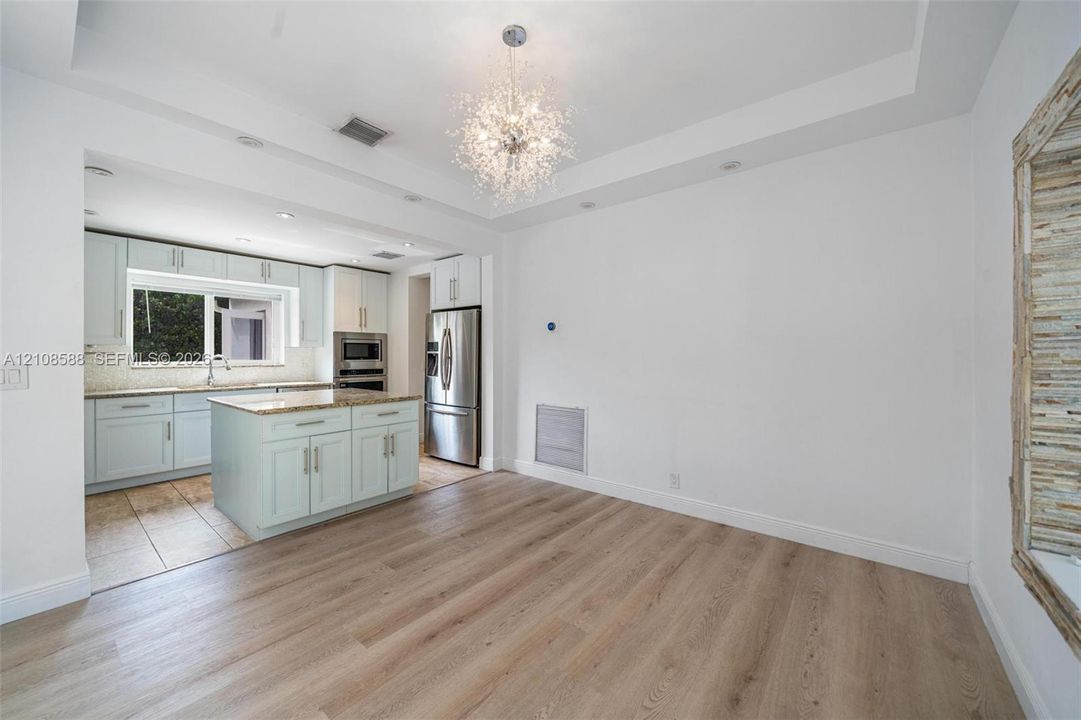 Tray ceiling with recessed lighting, central crystal-style chandelier, wood-finish flooring, kitchen island with stone countertop, and stainless steel appliances