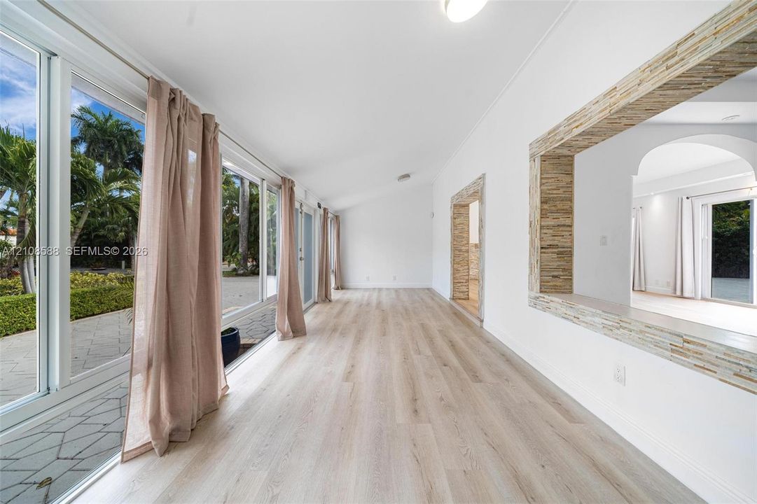 Light-filled interior featuring expansive floor-to-ceiling glass sliding doors, wood-finish flooring, a vaulted ceiling, and stacked-stone decorative trim surrounding the interior pass-through window