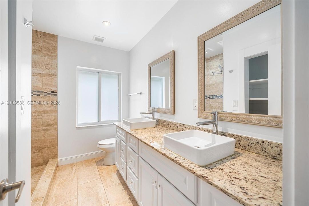 Double vanity featuring rectangular vessel sinks, stone-finish countertops, white cabinetry, and framed mirrors with a tiled shower enclosure
