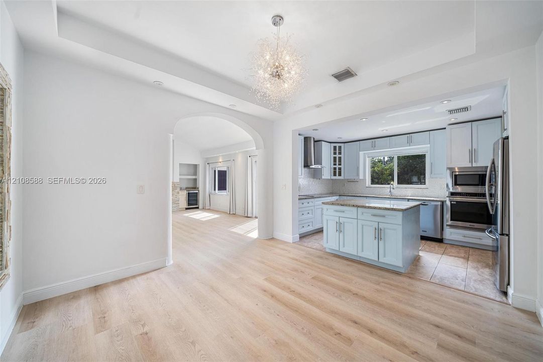 Kitchen featuring light blue cabinetry, stone countertops, stainless steel appliances, and a central island, punctuated by a tray ceiling with a contemporary pendant fixture and wood-finish flooring