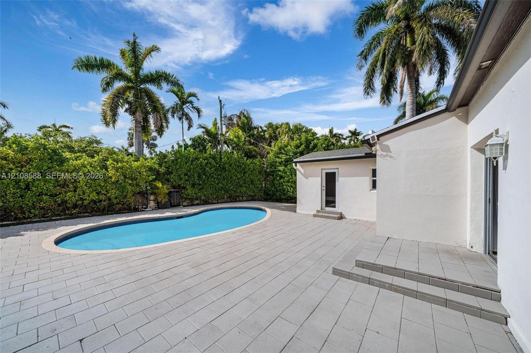 Expansive outdoor patio featuring light-toned concrete pavers, a kidney-shaped in-ground pool, and mature palm trees
