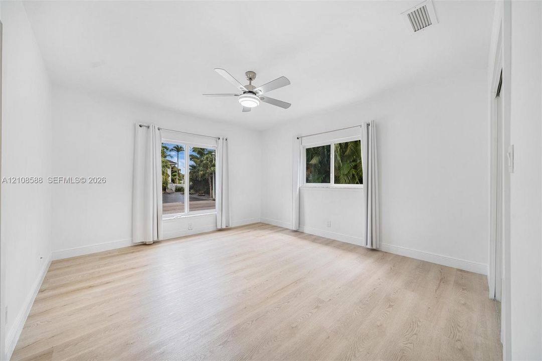 Room featuring light-toned wood-finish flooring, dual windows with exterior foliage, and a ceiling-mounted light fixture with a multi-blade fan