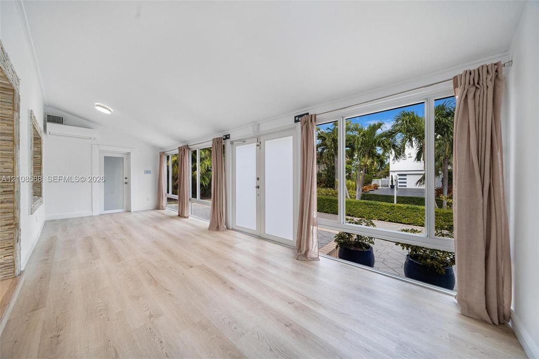 Sun-filled room featuring wood-finish flooring, a vaulted ceiling, floor-to-ceiling windows, and dual glass entry doors
